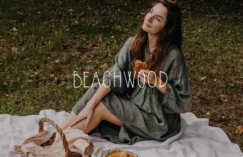 Woman sitting outdoors on a blanket, wearing a dress by Beachwood, evoking a bohemian and natural style.