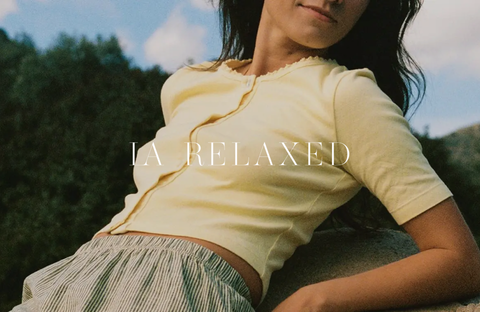 Woman wearing a light top by LA Relaxed, sitting in a natural environment, embodying relaxation and sustainable fashion.